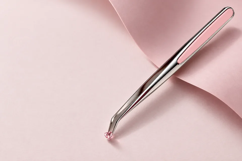 Pince tenant un petit cristal rose sur une surface de papier rose.